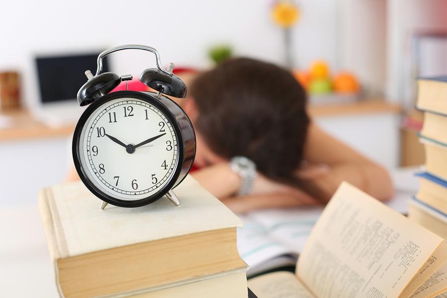 Tired female student at workplace in room taking nap on pile of textbooks. Sleepy brunette woman resting during education after sleepless night. Student in despair caused by exam deadline concept. Photo illustration purchased from BigStock.com.