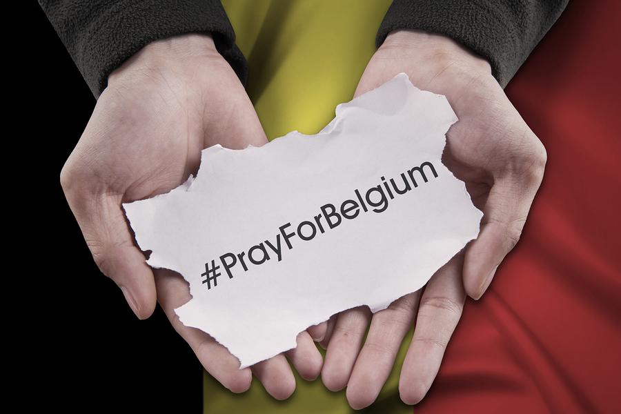 Close up of hands holding a paper piece with a text to pray for Belgium in front of Belgian flag