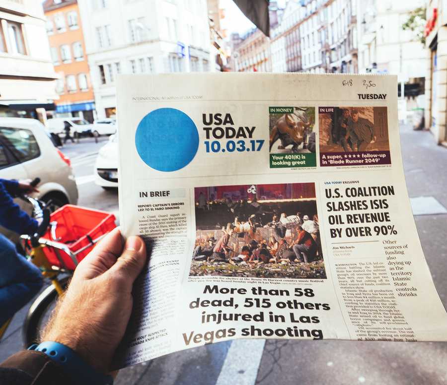 PARIS FRANCE - OCT 3 2017: Man buying USA Today newspaper with socking title and photo at press kiosk about the 2017 Las Vegas Strip shooting in United States with about 60 fatalities and 527 injuries