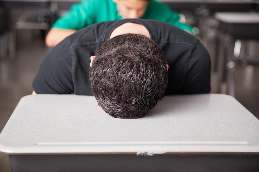 Portrait of a young high school student bored and frustrated with his head down on his desk