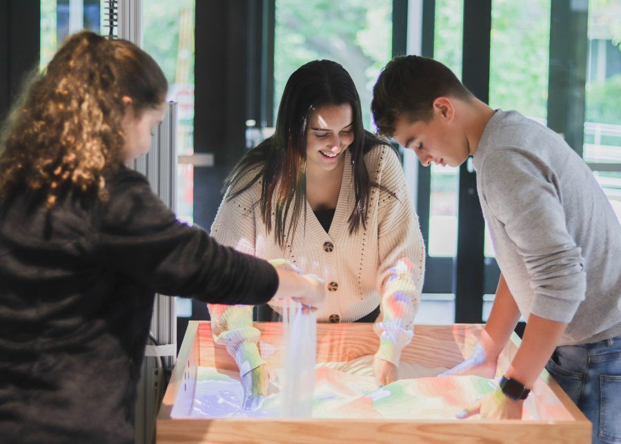 Talia Hammer, Sylvia Tejada, and Owen Williams ’23 create a meandering river basin system with tributaries and deltas using the new Augmented Reality sandbox.