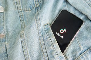 The TikTok logo on a smartphone screen sticks out of the pocket of a denim jacket. Photo illustration. 