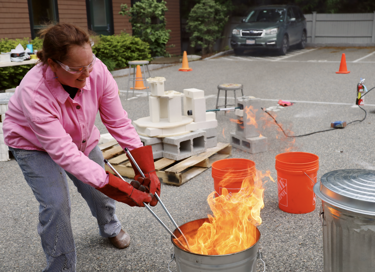teacher Amy Carpenter skillfully handles a ceramic piece during the Raku firing session, highlighting the exciting and intense nature of this traditional technique.